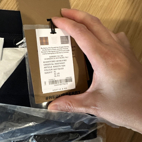 Hand holding a Burberry tag with product details on a wooden surface