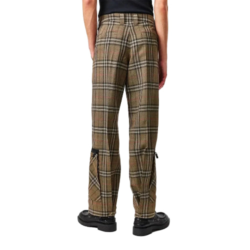 A person shown from the back wearing plaid trousers in brown, beige, and black, paired with black shoes, against a light gray studio background.