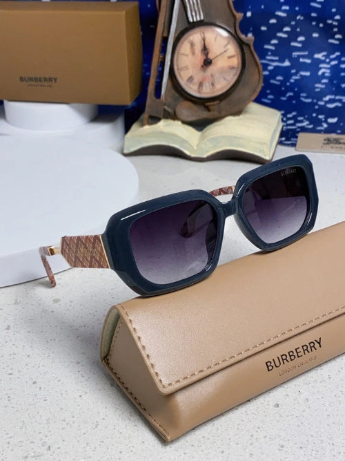Burberry sunglasses with a dark navy blue frame, gradient purple lenses, and a woven beige patterned temple, resting on a tan Burberry leather case.