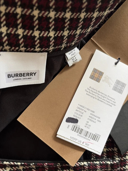 Close-up of a Burberry garment showing the interior label, hangtag, brown paper packaging, and a tartan pattern in burgundy, beige, and black.