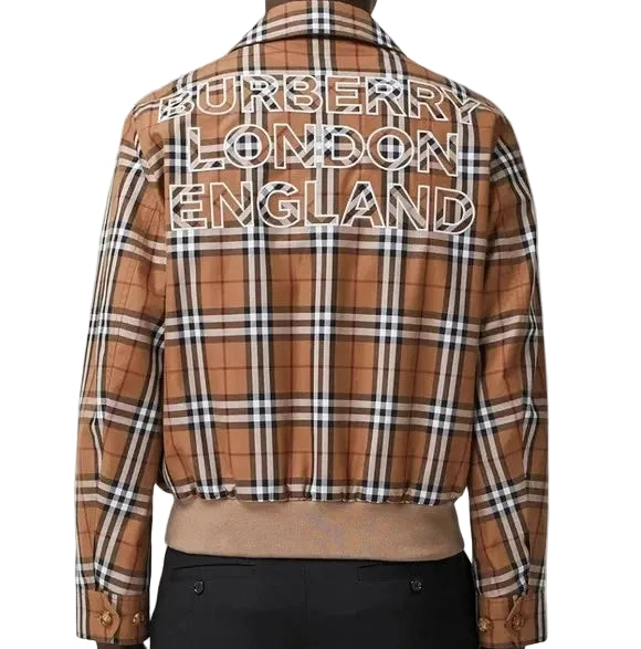 A cropped Burberry plaid jacket shown from the back, featuring the text 'BURBERRY LONDON ENGLAND' printed across the shoulders in white outlined lettering. The jacket has a classic brown, beige, and black check pattern and is styled with black trousers against a light gray background.