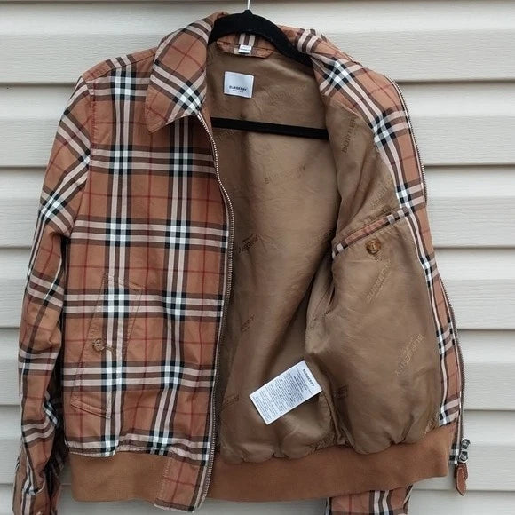 A vintage Burberry plaid jacket in brown, beige, and white, shown open on a black hanger against a white siding background. The jacket features a classic check pattern on the front and sleeves, a solid brown collar, and a brown lining.
