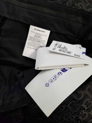 A close-up of a black garment, likely a denim jacket or sweatshirt, showing a white inner label and a white paper tag with blue text.