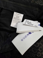 A close-up of a black garment, likely a denim jacket or sweatshirt, showing a white inner label and a white paper tag with blue text.
