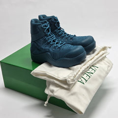A pair of dark blue high-top athletic boots displayed on top of a green box and white drawstring bag with green branding.