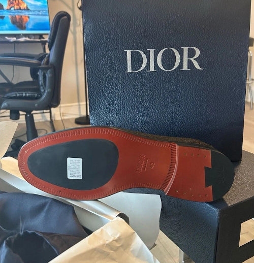 Dior shoe with red sole on a black Dior box in an office setting