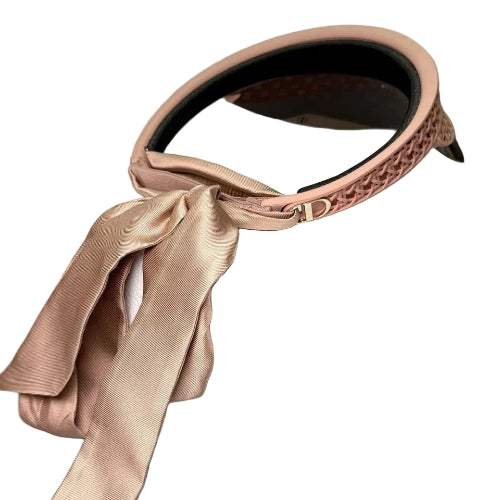 A blush pink woven headband with a matching satin ribbon bow, displayed on top of a white Dior box.