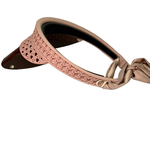 A blush pink visor hat with a floral lace pattern on the crown, a matching satin ribbon tie, and a dark brown glossy visor, displayed on a white textured box.