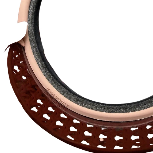 A close-up of a hand holding a large round mirror with a beige inner rim, a dark gray textured inner layer, and a reddish-brown ornate outer frame. A nude-colored garment is draped over the mirror, and the words 'MADE IN ITALY' are visible on the beige rim.