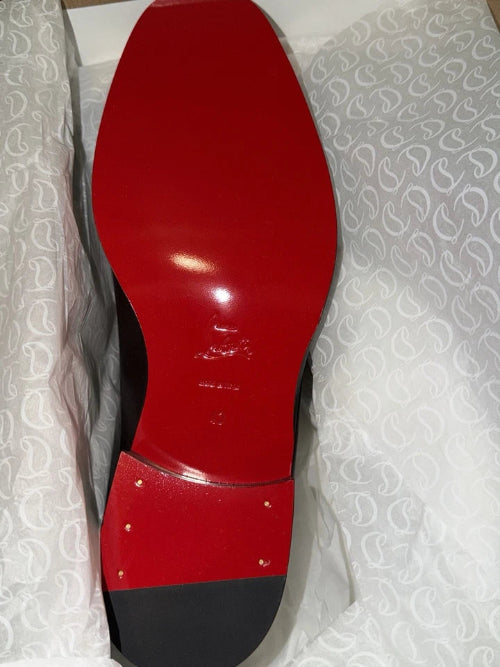 A close-up of a red and black shoe sole, showing a glossy red heel counter and black midsole, photographed against a white textured background.