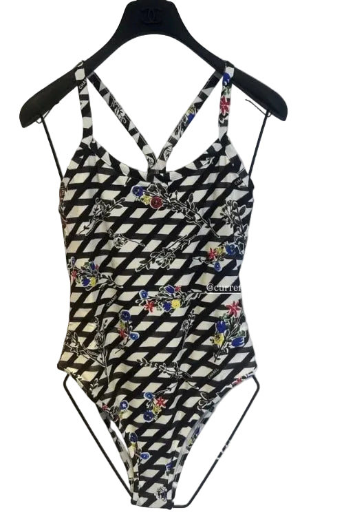 A black and white patterned one-piece swimsuit with a halter-style neckline and cutout sides, hanging on a black hanger against a light-colored wall.