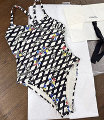 A black and white patterned one-piece swimsuit laid flat on a white surface, with a small black-and-white accessory visible at the side.