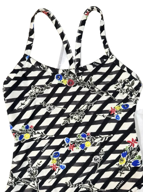 A black and white geometric patterned halter top with colorful floral embroidery, laid flat on a wooden surface next to a white Chanel bag.