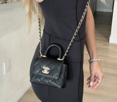 Person wearing a black dress with a quilted handbag featuring the Chanel logo.