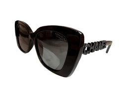 Black CHANEL oversized cat-eye sunglasses with dark lenses, displayed on a white stand with a black CHANEL box in the background.
