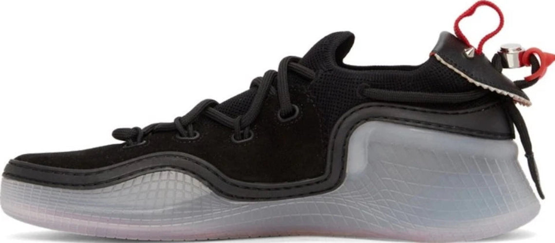 A black low-top sneaker with a thick translucent gray and white sculpted sole, black laces, and a red pull tab on the heel.