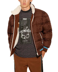 Person wearing a brown patterned jacket with white lining, a dark t-shirt with graphic design, and brown pants on a light gray background.