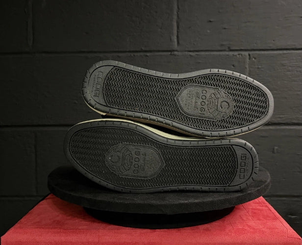 Black shoes with soles facing up on a red surface against a dark brick wall.