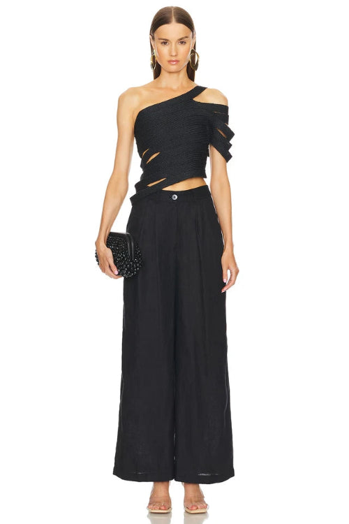 Woman wearing a black one-shoulder top and wide-leg pants on a white background