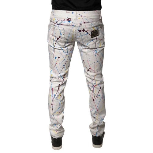 White slim-fit jeans with a colorful paint splatter print, shown from the back on a model wearing a black shirt and black sneakers.