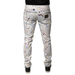 White slim-fit jeans with a colorful paint splatter print, shown from the back on a model wearing a black shirt and black sneakers.