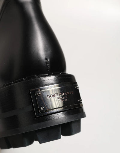 Close-up of a black leather boot with a chunky lug sole and a silver-tone metal plaque engraved with 'DOLCE&GABBANA MILANO ITALY'.