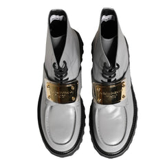 A pair of metallic silver ankle boots with black soles and a prominent gold buckle detail on the sides, shown against a plain white background.