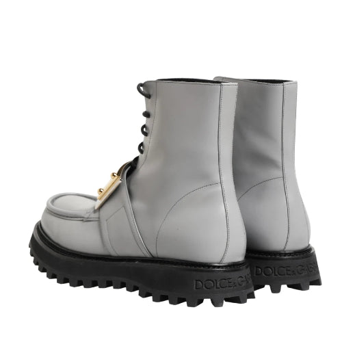 A pair of light gray lace-up boots with chunky black lug soles and a small gold buckle detail, shown against a plain white background.