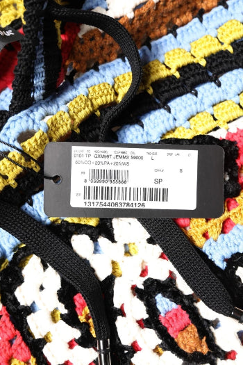 Close-up of a colorful crocheted or knitted textile with black drawstrings and a black product tag attached, showing a multicolor pattern in blue, yellow, black, white, and red.