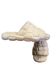 White sandals with a brand logo held by a hand on a gray surface