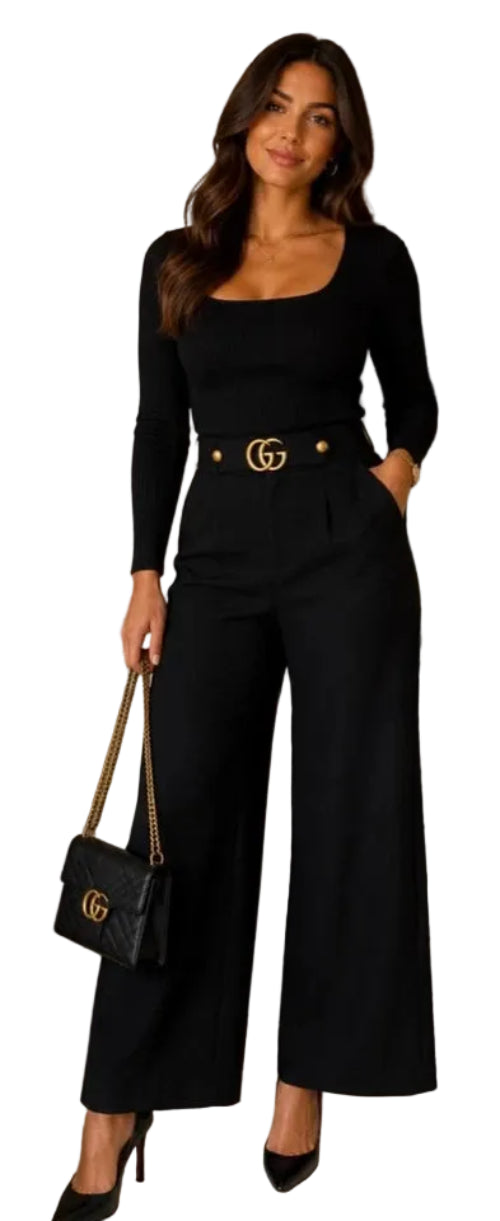 A woman modeling a black long-sleeve jumpsuit with a square neckline, wide legs, and a gold double-G buckle belt. She is holding a black quilted Gucci handbag with a gold chain strap in an indoor setting.