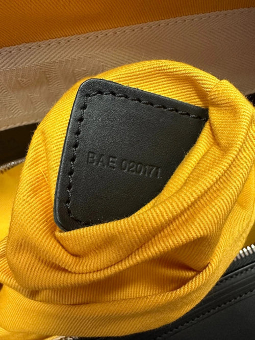 Close-up of a yellow fabric pouch or organizer inside a black bag, showing a black leather tab stamped with the code 'BAE 020171'.