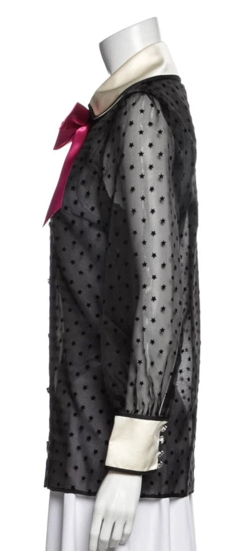 Black polka dot blouse with white cuffs and pink bow on a mannequin against a white background