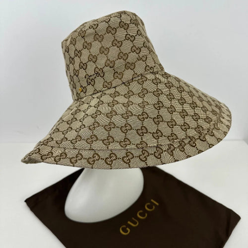 A beige and brown monogram patterned wide-brimmed sun hat displayed on a white mannequin head with a dark brown Gucci box underneath, on a white background.