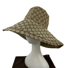 A Gucci bucket hat in the signature GG monogram canvas, displayed on a white mannequin head. The hat features a beige and brown GG pattern, photographed against a plain white background with a dark brown surface visible at the bottom.