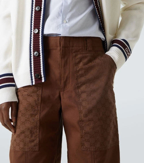 A close-up of a person wearing brown corduroy trousers, a white shirt, and a cream-colored jacket with navy and red stripes on the sleeves.