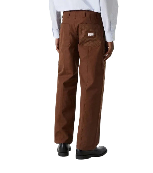 A person shown from the back wearing brown work pants and black shoes against a plain light gray studio background.
