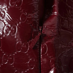 Close-up of a glossy burgundy quilted jacket featuring an embossed Gucci GG monogram pattern and a matching zipper pull with the word 'GUCCI'.