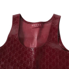 Close-up of a Gucci sleeveless top in glossy embossed GG Supreme leather in a deep burgundy red, showing the inner neck label with 'GUCCI MILAN'.