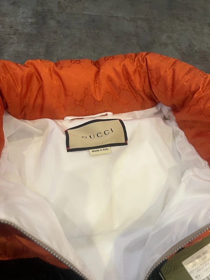 Close-up of an orange puffer jacket with a Gucci label on a gray background