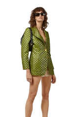 Woman wearing a green patterned blazer over a sheer top on a white background