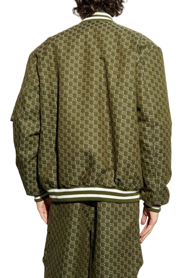 A person shown from the back wearing an olive green bomber jacket and matching pants with a repeating geometric monogram pattern and striped ribbed collar, cuffs, and hem.
