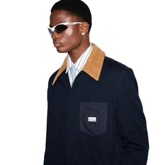 Person wearing a dark coat with a tan collar and sunglasses on a plain background