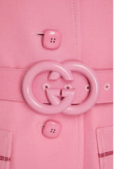 Close-up of a pink coat with a large circular button and two smaller buttons on a matching pink background.