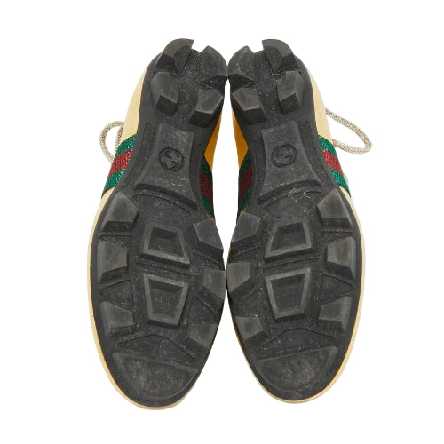 The soles of a pair of Gucci sneakers, showing the black treaded rubber and the iconic green and red web stripe on the sides, photographed from above on a white background.