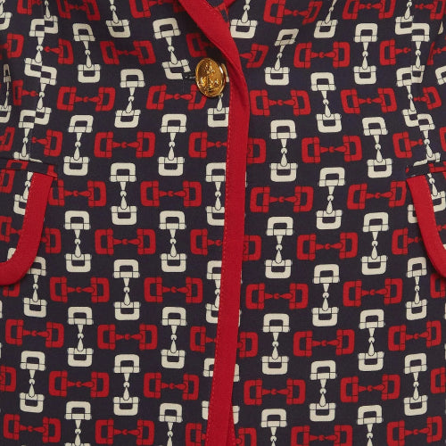 Close-up of a patterned fabric garment featuring a navy blue base with a repeating red and white horsebit motif, accented by a red trim and a gold-tone button.