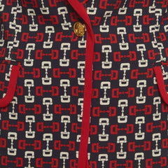 Close-up of a patterned fabric garment featuring a navy blue base with a repeating red and white horsebit motif, accented by a red trim and a gold-tone button.