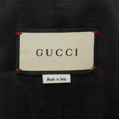 A close-up of a Gucci label on black fabric, with the Gucci brand name clearly visible on the cream-colored rectangular label.