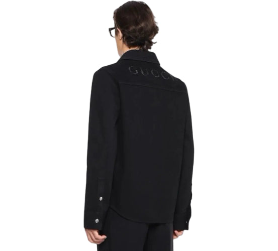 A model shown from the back wearing a black Gucci shirt jacket with the brand name embroidered across the shoulders, set against a plain white background.