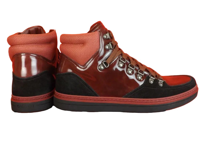 Brown and black high-top sneakers with silver studs on a Gucci box against an orange background